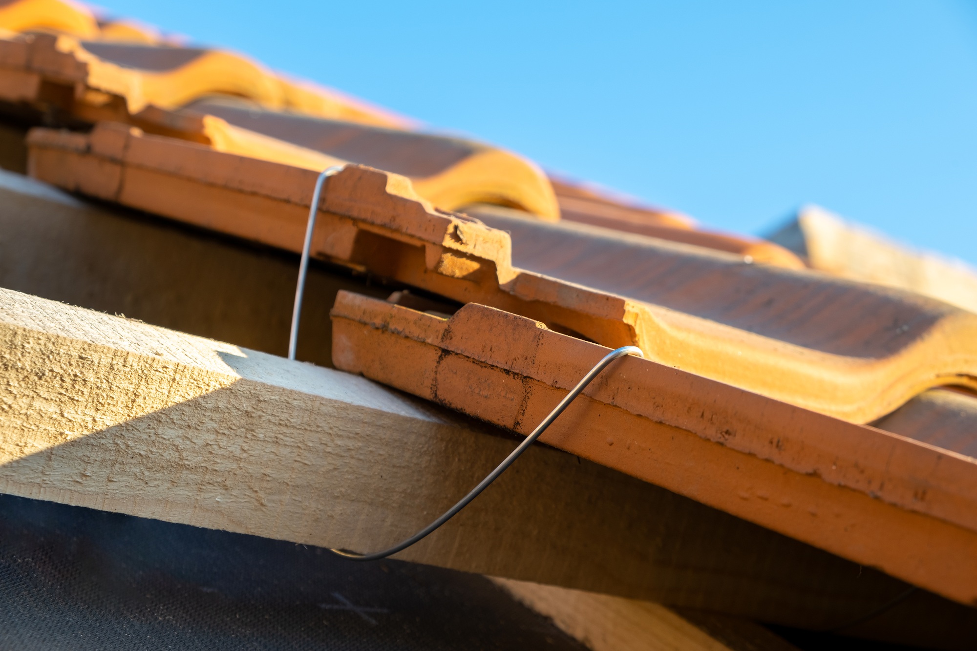 Closeup of metal montage anchor for installation of yellow ceramic roofing tiles mounted on wooden